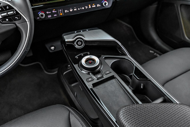 Jednou z výrazných předností nového typu Kia EV6 je rovná podlaha v celé délce interiéru. Zcela chybí středová konzola. Vpředu je díky tomu dostatek prostoru pro kolena pod panelem s otočným ovladačem směru jízdy a v jeho okolí se nachází množství různých odkládacích schránek včetně přihrádky na bezdrátové nabíjení telefonu.