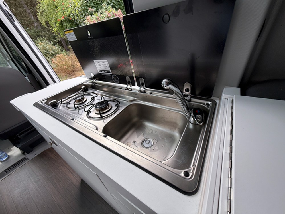 Pod umyvadlem a vařičem se nachází několik prostorných úložných skříněk. Po obou stranách jsou výklopné desky