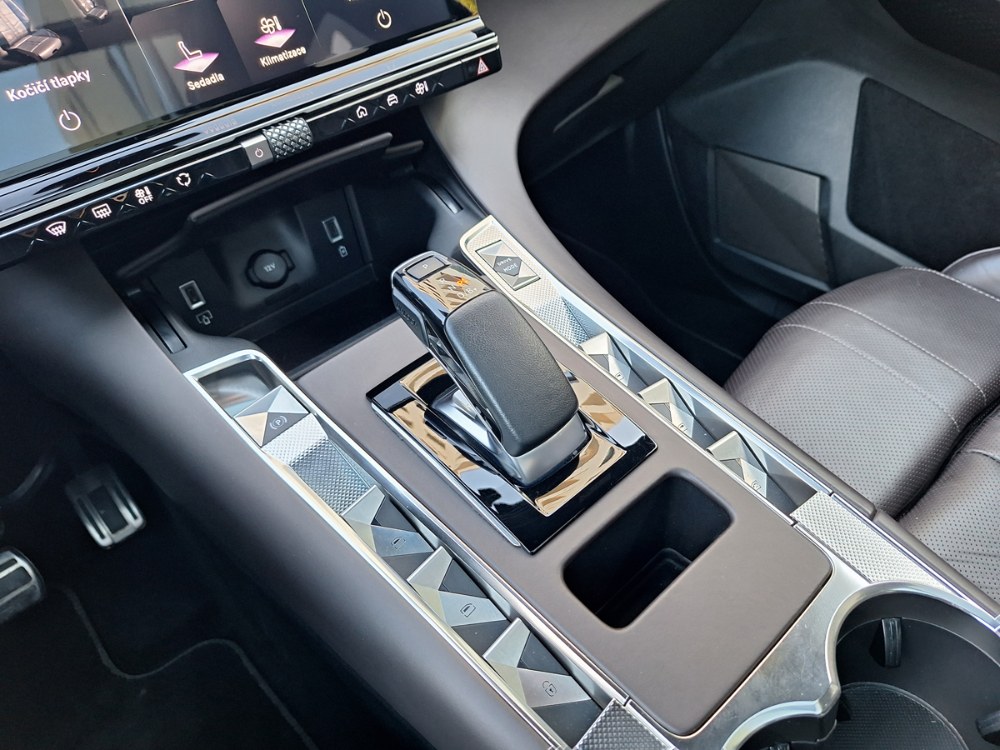 Středová konzola nese dokonale funkční volič převodovky. Vpravo od něj je přepínač provozních režimů, po stranách tlačítka spouštění dveřních skel