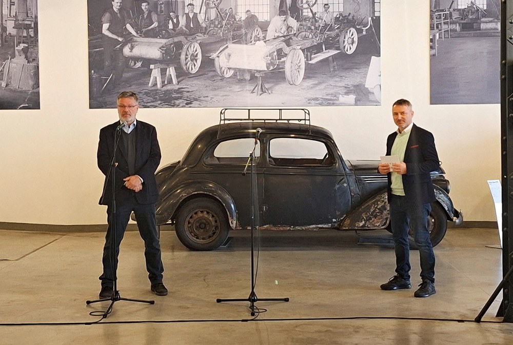 Michal Velebný, vedoucí restaurátorské dílny Škoda Muzea, představuje celý projekt a jednotlivé exponáty. Vpravo Vítězslav Kodym, současný šéf komunikace produktu Škoda Auto a náš průvodce slavnostním otevřením depozitáře. Stěny haly V4 zdobí efektní zvětšeniny fotografií z dob, kdy se zde automobily vyráběly